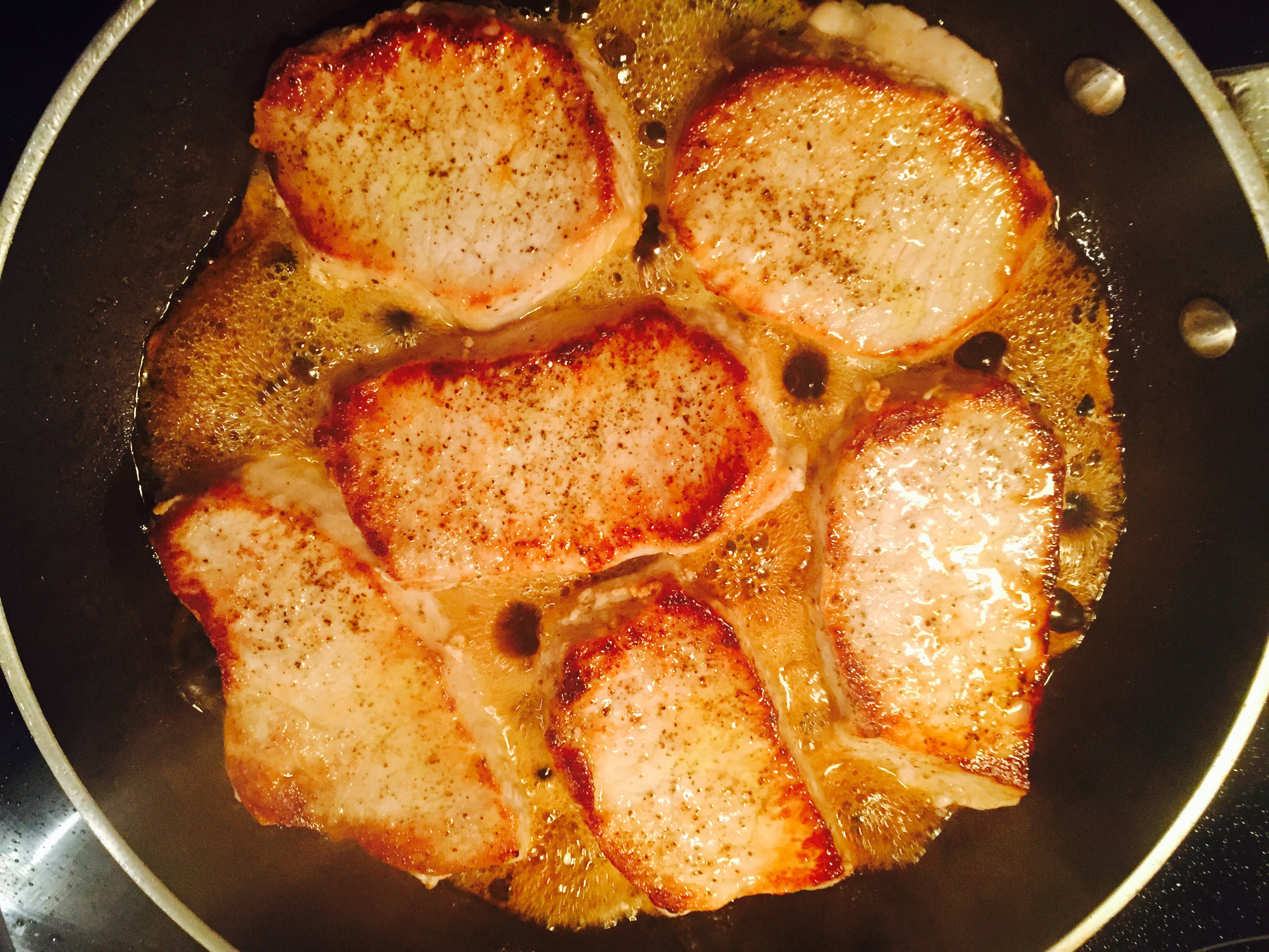Seasoned organic pork chops being seared in a non-stick pan