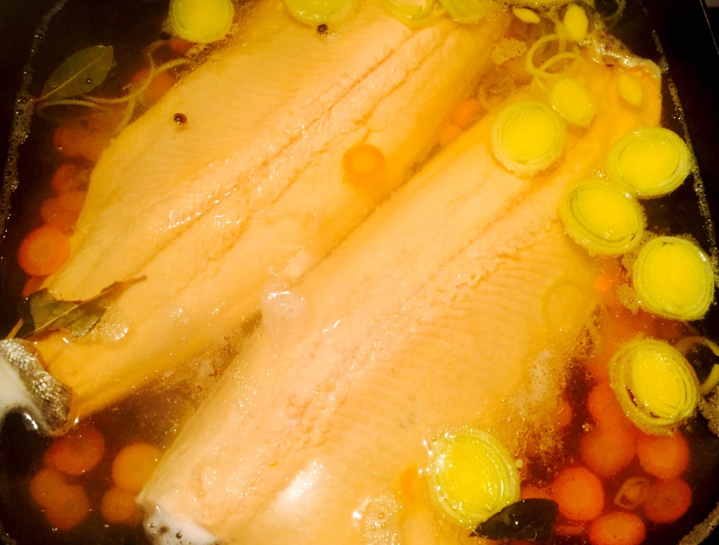 Fresh trout simmering in a warm poaching liquid with vegetables, bay leaf and peppercorns